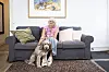 Jena Krogslykke sidder på en grå sofa i stuen med sin hund foran sig på gulvtæppet.