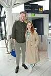 Par står og smiler foran gate A9 med afgangsskilt mod Sønderborg i lys lufthavnsterminal.