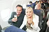 Par i flysæder løfter glas med mousserende vin på et fyldt passagerfly