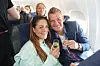 To flypassagerer skåler med mousserende vin i deres sæder i en fyldt flykabine.