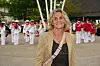 Smilende kvinde foran orkester i røde og hvide uniformer ved Strax-arrangement.