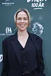 Person i mørkt jakkesæt foran grøn væg med Nordisk Film‑logo ved jubilæumsarrangement.