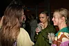 Tre personer står og taler med drinks i hånden ved et arrangement indendørs.