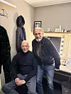 To mænd poserer ved et oplyst sminkebord i et lille omklædningsrum