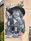 Sort-hvidt murmaleri af Tove Ditlevsen og to børn på trappe med blomster på facade i bymiljø.