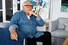 Flemming Østergaard sidder i en sofa i en lys stue med kunst på væggene
