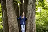 Sara Lygum står mellem flere træstammer i en frodig grøn skov
