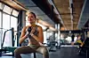Kvinde i sportstøj laver squat med kettlebell i et lyst fitnesscenter.