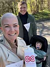 Smilende voksen med indsamlingsbøtte fra Kræftens Bekæmpelse foran barnevogn udendørs.