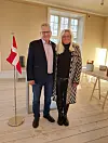 Par står i lys stue ved dansk flag og borde under stort vindue