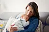 Mor sidder i sofaen og holder sin nyfødte baby tæt ind til sig