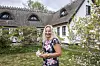 Kvinde i mønstret kjole står i have foran hvidt stråtækt hus