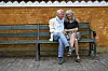 Gina Bakke og Erik Vilen sidder smilende på en bænk ved en okkergul mur i Frederiksberg Have.