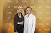 To kvinder står foran gylden Triangle of Sadness-fotovæg ved filmpremiere