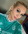 Kvinde i grøn Liverpool FC-fodboldtrøje poserer til nærbillede indendørs.