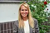 Smilende kvinde i grå blazer ved bogreception foran mur og roser.