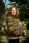 Gravid kvinde med krøllet hår står udendørs og holder om sin mave.