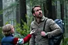 Mand med rygsæk og dreng med lille enhed står i en tæt grøn skov
