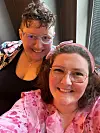 To smilende personer med briller i farverigt tøj poserer tæt til kameraet indendørs.