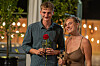 To unge voksne holder champagneglas og en rød rose på en terrasse om aftenen.
