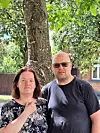 To voksne står foran et træ i et grønt boligområde i solskin