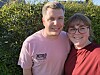 Smilende par står skulder ved skulder foran en grøn hæk i solskin