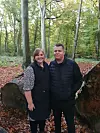 To personer i mørkt tøj står i en efterårsskov foran en fældet træstamme