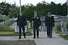 Tre officerer i paradeuniform går side om side på en sti ved et militært anlæg.