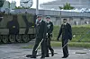 Tre officerer i uniform går med sabler forbi et pansret køretøj på en kaserne