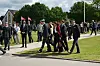 Uniformerede personer og civile går ved en udendørs Strax-ceremoni med dannebrog.