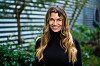 Rikke Gøransson står udendørs foran en bygning med grøn beplantning.