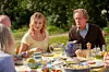 Margot Robbie og Bill Nighy, der sidder ved et udendørs bord dækket med mad og drikke i solskinsvejr.