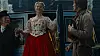 Margot Robbie træder ud af blå hestevogn i historisk kostume mellem to andre personer.