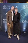 Par står på den røde løber foran Vores løfte-fotovæg ved filmpremiere.