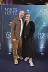 Par står på den røde løber foran Vores løfte-fotovæg ved filmpremiere.