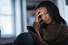 Kvinde sidder alene og græder, mens hun læser en besked på sin smartphone.