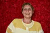 Smilende person med briller foran rød blomstrende bagvæg ved Bachelorette 2026-finalen