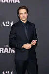Robert Pattinson i mørk habit foran A24-væggen ved premieren på 'The Drama'.
