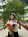 Ung person med studenterhue holder farverige blomster i lys indendørs aula.