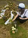 Ung kvinde med studenterhue lægger blomster ved gravsted med lys og buketter