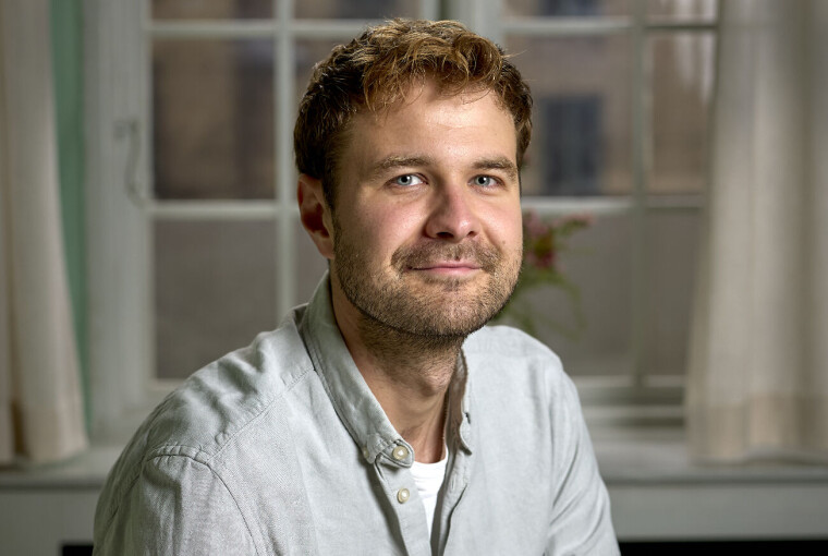 Magnus Haugaard sidder ved et bord i et lyst lokale med vindue og gardiner bag sig.