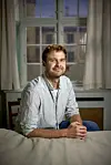 Magnus Haugaard sidder ved et bord i et lyst lokale med vindue og gardiner bag sig.
