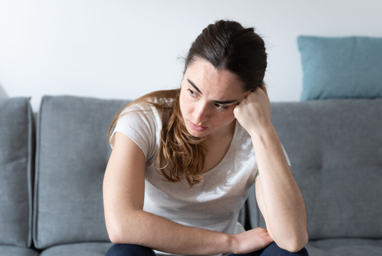 Ung kvinde sidder alene i sofa og ser trist og bekymret ud