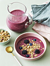 Skål med pink smoothiebowl toppet med granola, blåbær og brombær ved siden af kande smoothie.