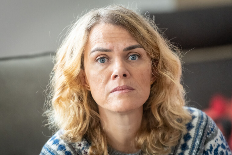 Moden kvinde med alvorligt udtryk sidder indendørs og ser ind i kameraet.