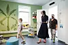 Voksne og barn træder ind i et lyst hospitalsrum med grøn vægdekoration