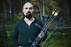 Mand holder compoundbue med pile i en grøn skov