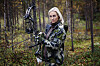 Kvinde i camouflagetøj holder en compoundbue i en tæt skov