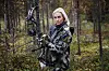 Kvinde i camouflagetøj holder en compoundbue i en tæt skov
