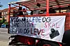 Rød åben lastvogn med studerende og stort håndmalet banner parkeret ved fortov i solskin